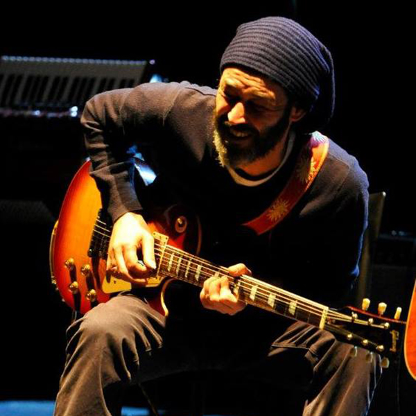 Foto a colori con primo piano di un uomo che si sta esibendo con un berretto alla chitarra durante un'esibizione