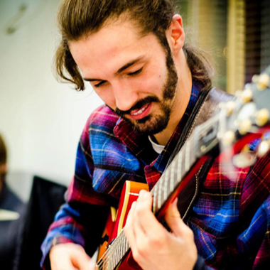 Foto a colori con primo piano di un ragazzo sorridente che si sta esibendo alla chitarra durante un'esibizione